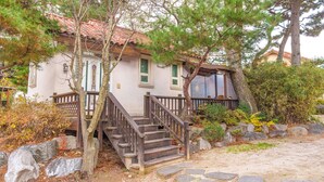 A traditional house with a wooden staircase leading to a porch, surrounded by trees and rocks. - Gyeongju Clearmorning Petfriendlypension (Gyeongju)