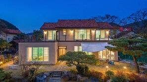 A two-story house with a red-tiled roof, large windows, and a well-lit garden with rocks and plants. - Gyeongju Clearmorning Petfriendlypension (Gyeongju)