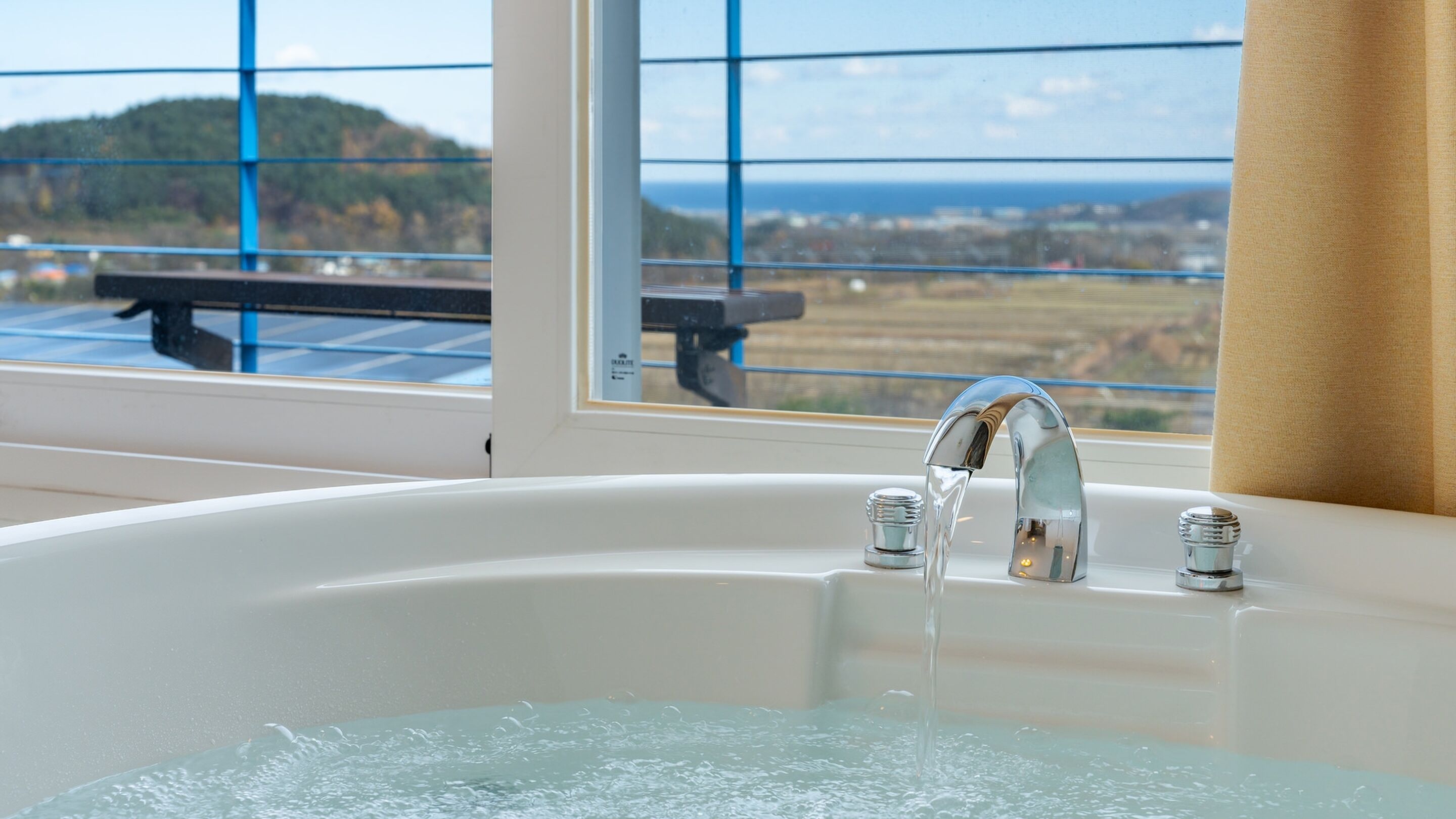 Una bañera con agua corriente, una ventana con vistas al paisaje y una cortina a la derecha.