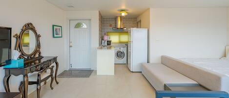 A compact room with a bed, a desk, a mirror, a washing machine, and a refrigerator.