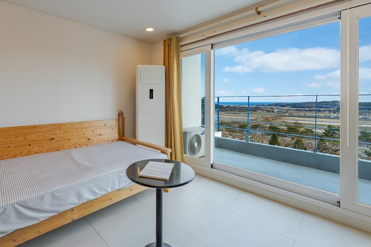 Une petite pièce avec un lit en bois, une petite table et une grande fenêtre donnant sur un paysage.