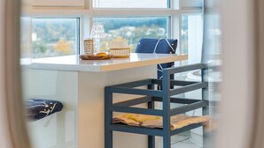 Una cocina moderna con encimera blanca, una silla azul y vistas al exterior a través de amplios ventanales.