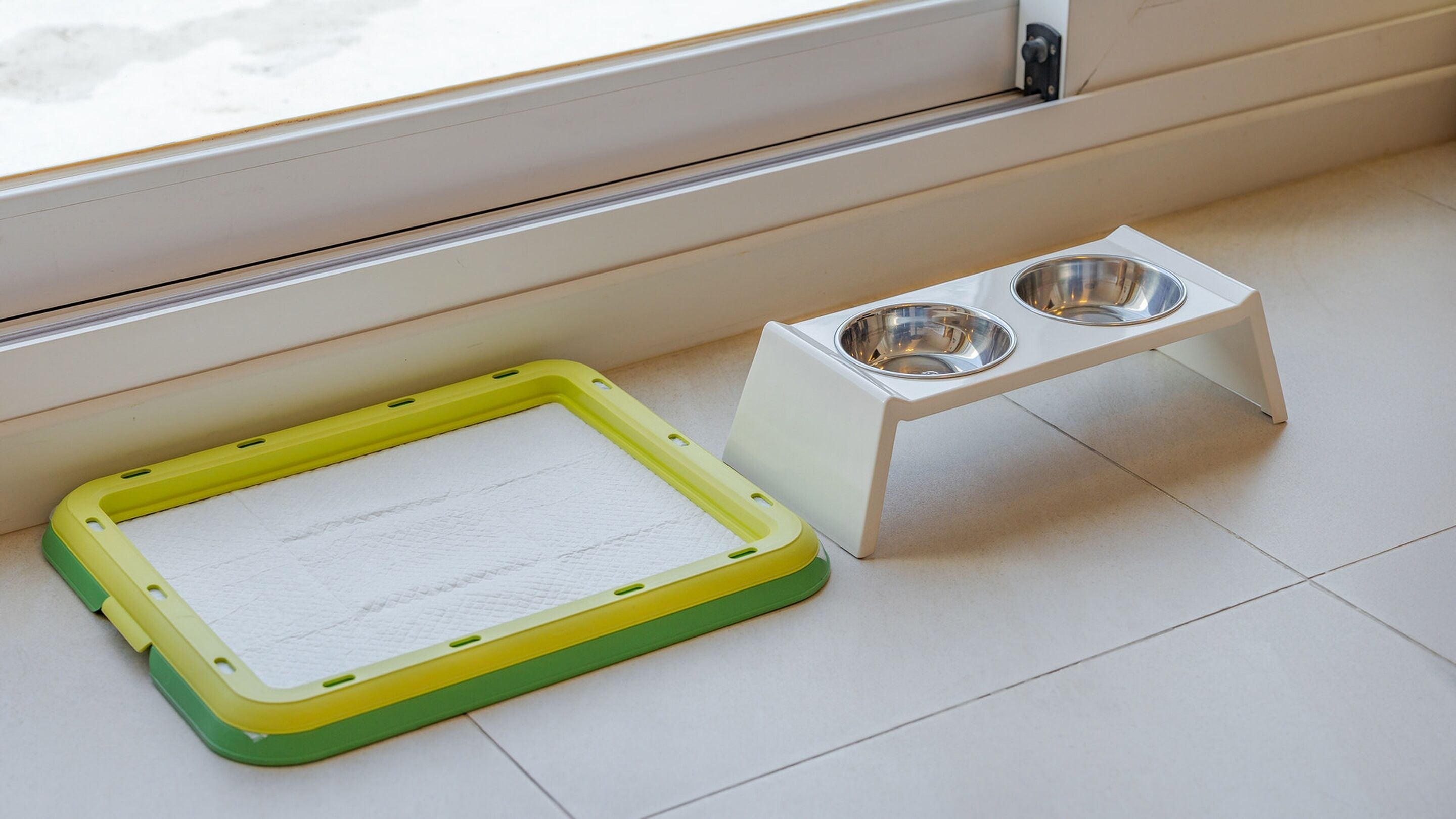A pet feeding area with a yellow and green mat and a white stand with two metal bowls.