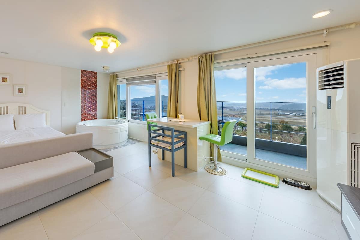 Une chambre d’hôtel moderne équipée d’un lit, d’un canapé, d’une petite table, d’une chaise, d’une baignoire et de grandes fenêtres donnant sur la ville.