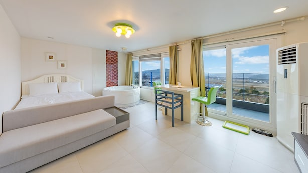 Una habitación de hotel moderna con cama, sofá, una mesita, una silla, bañera y ventanas amplias con vistas a la ciudad.