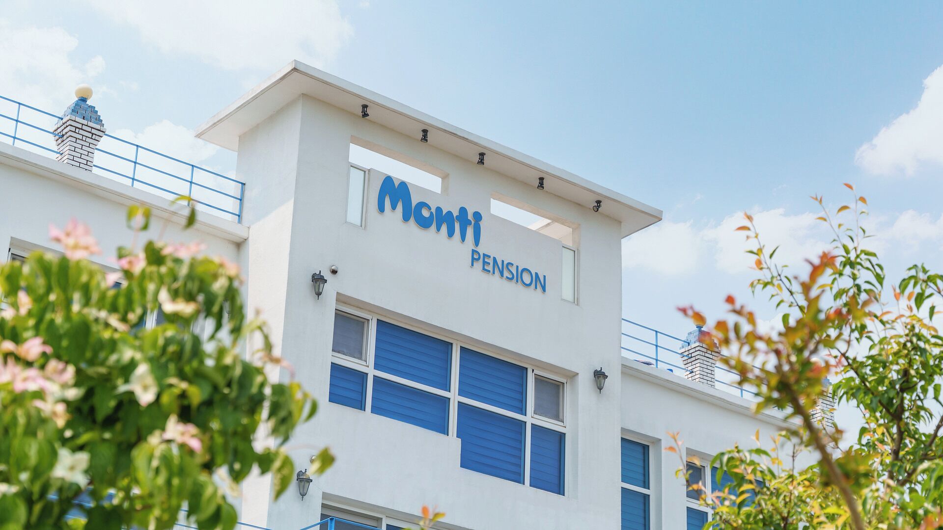 Un immeuble sur lequel on peut lire l’inscription « Monti Pension », et qui présente un style architectural moderne, avec un toit plat et de grandes fenêtres.