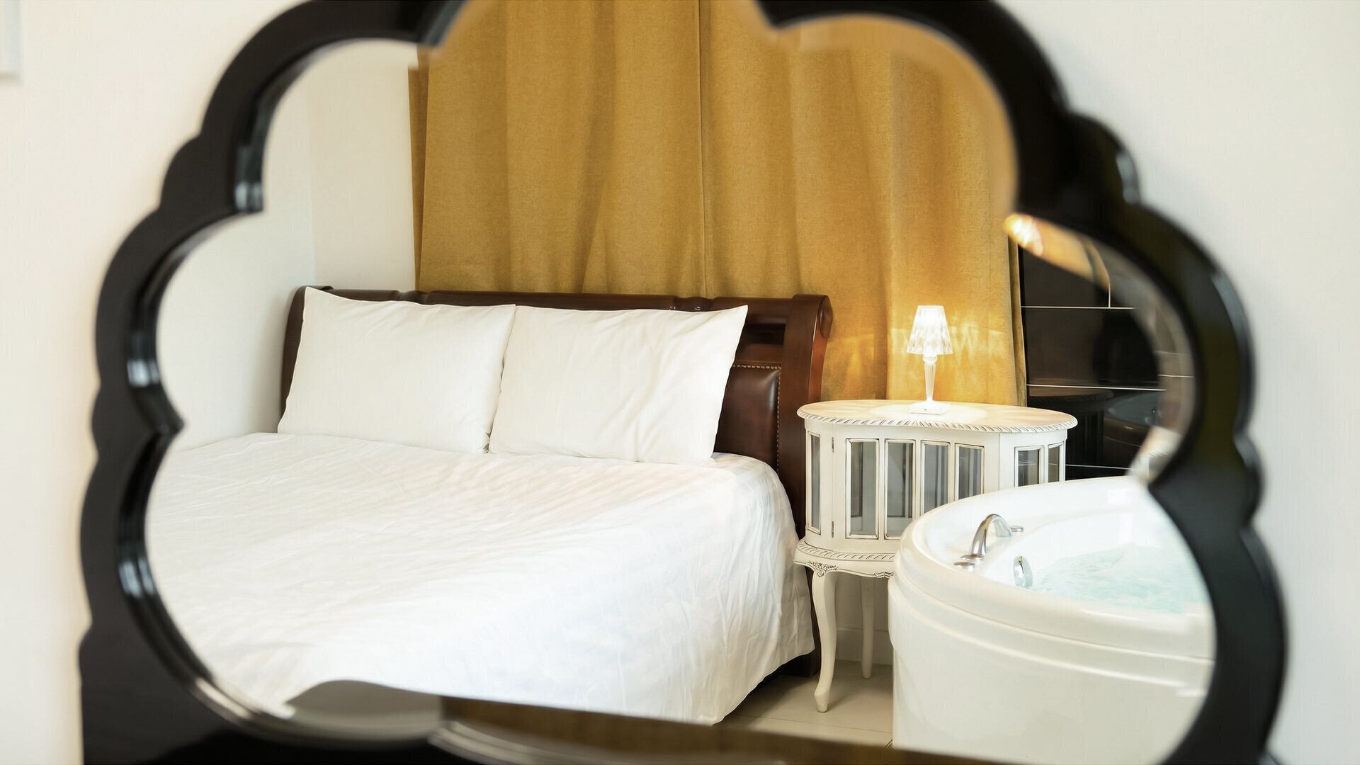 Una habitación de hotel con cama, mesita de noche, lámpara y bañera.