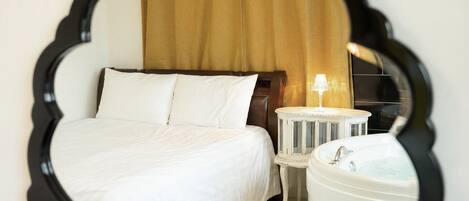 Una habitación de hotel con cama, mesita de noche, lámpara y bañera.