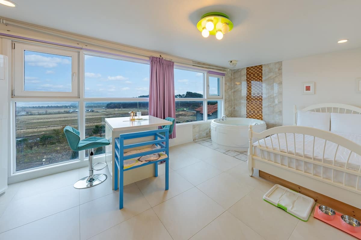Une chambre à coucher comprenant un lit, un bureau, une chaise, une baignoire et donnant sur la campagne.