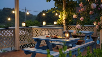 Un espacio de comedor al aire libre con mesas y bancos de madera, luces colgantes y un farol.