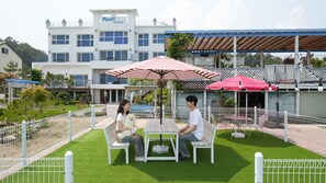 A patio area with a white table and bench, surrounded by a white fence and green artificial grass. - Yangyang Monti Pet Spa Pension (Yangyang)