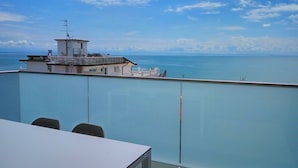 Un balcon avec vue sur la mer et un bâtiment surmonté d’un mât portant un drapeau.