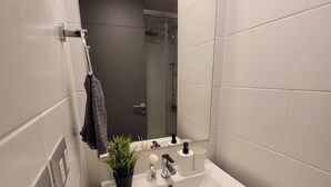 Uma casa de banho moderna com uma sanita branca, um espelho, um porta-toalhas e uma área de duche.