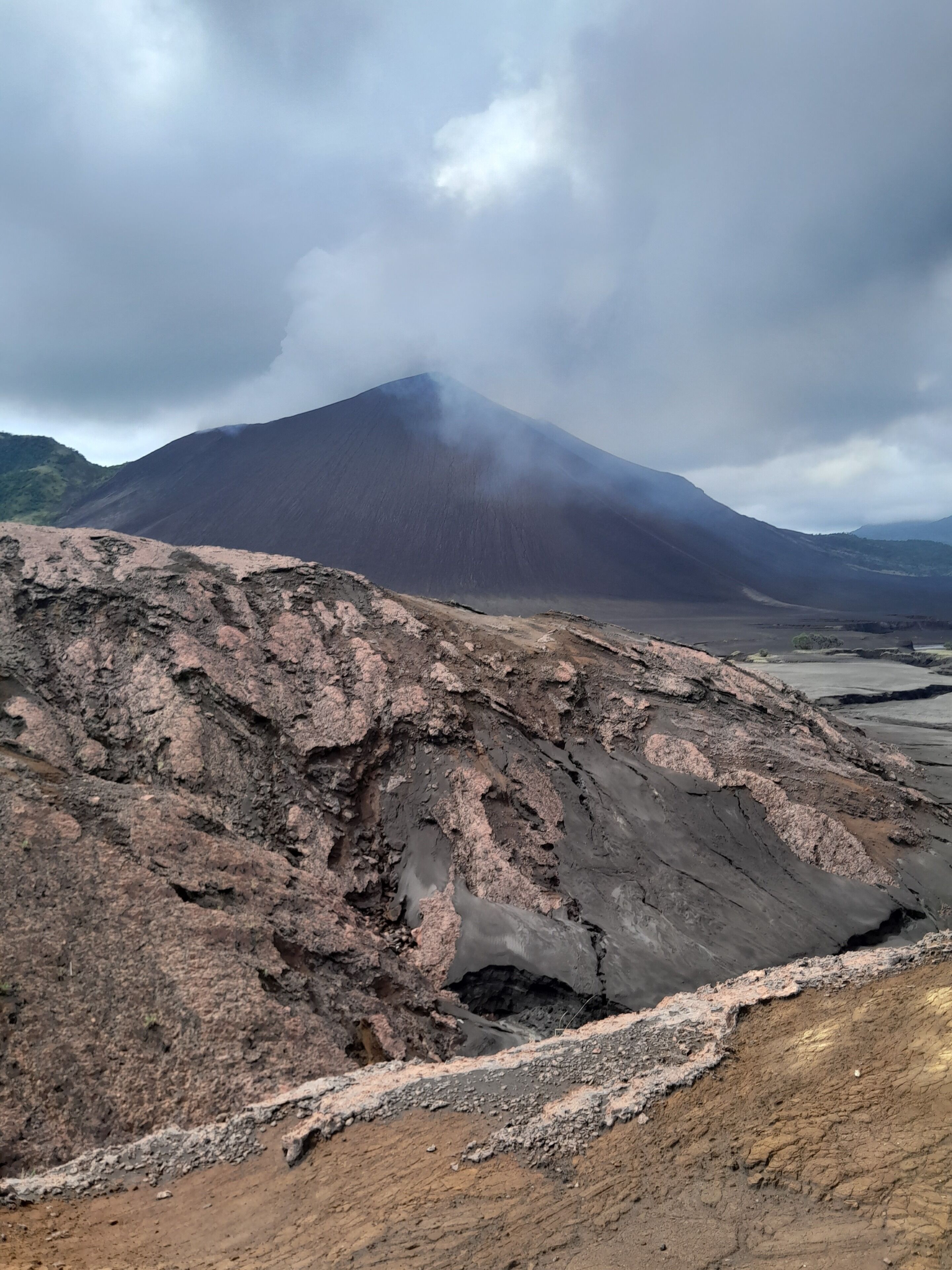 Een vulkanisch landschap met een opvallende berg op de achtergrond.