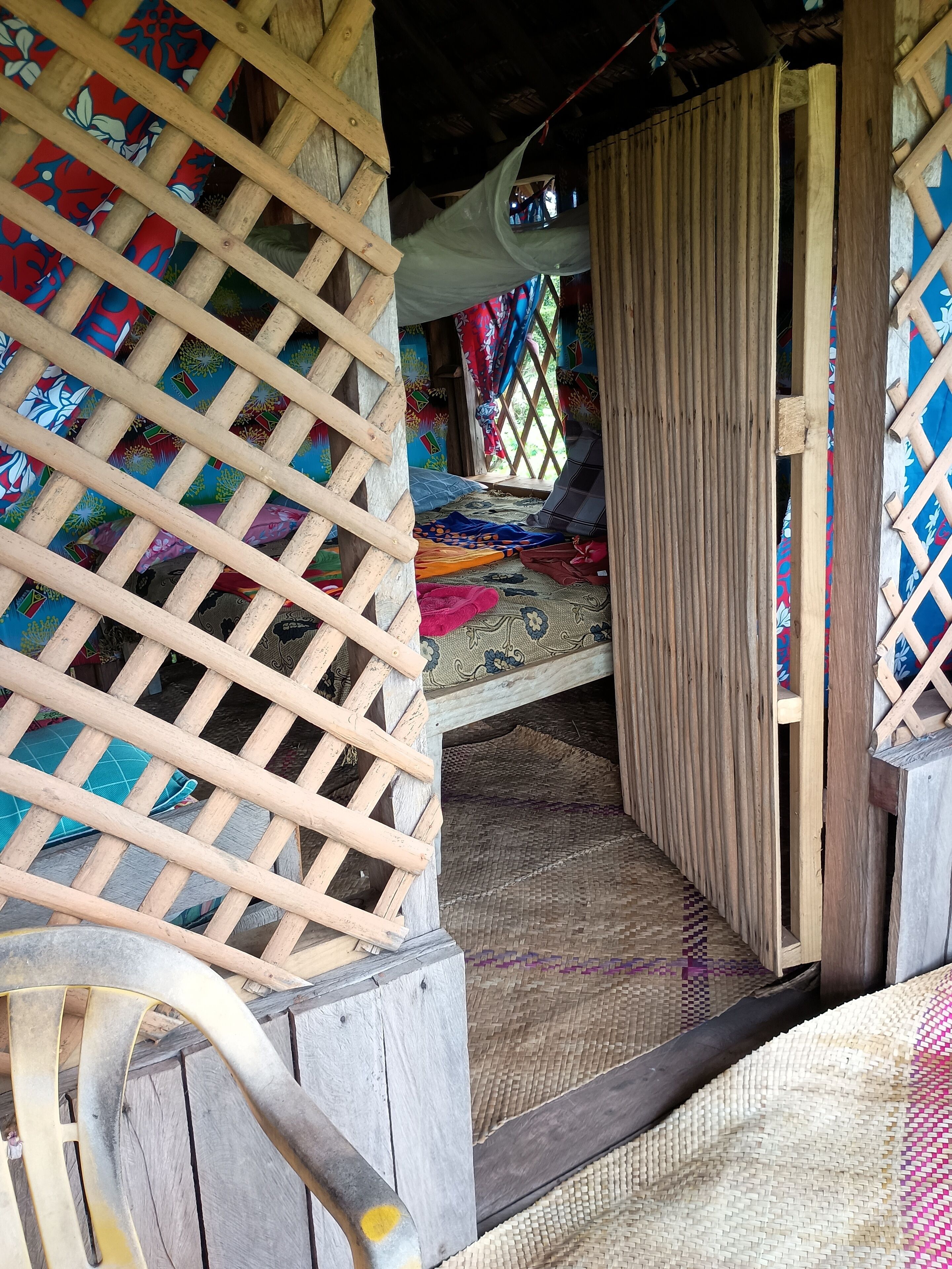 A room with a bed, a wooden lattice partition, and a woven mat on the floor.