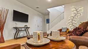 A modern living room with a round coffee table, a brown leather sofa, a flat-screen TV, and a staircase leading to another level.