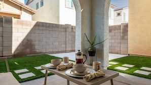 An outdoor dining area with a table set for two, a coffee pot, and a potted plant.