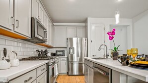A modern kitchen with white cabinets, stainless steel appliances, and a wooden floor.