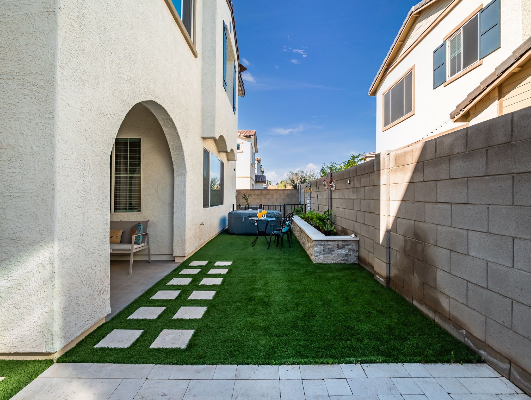 A courtyard with artificial grass, a stone bench, and a small seating area with a table and chairs.