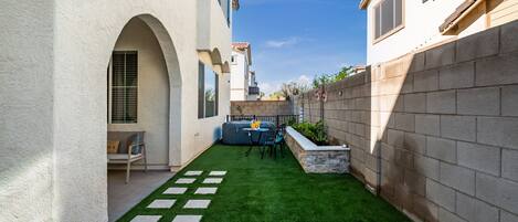 A courtyard with artificial grass, a stone bench, and a small seating area with a table and chairs.