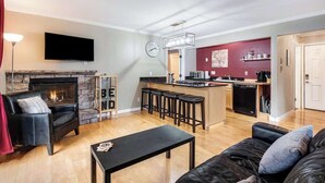 Una sala de estar con chimenea, televisor y una zona de cocina con barra.