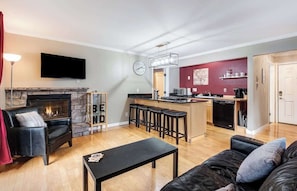 Una sala de estar con chimenea, televisor y una zona de cocina con barra.