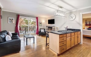 A modern living room with a black leather sofa, wooden dining table, and a kitchen island with wooden cabinets. - Park Side Getaway! Walk to Downtown & Trails (Bend)