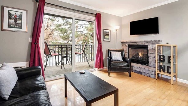 Una sala de estar con chimenea, televisor, sofá, mesa de centro y balcón con cortinas rojas.