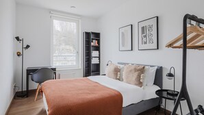 A modern bedroom with a bed, a desk, a chair, a wardrobe, and a window.