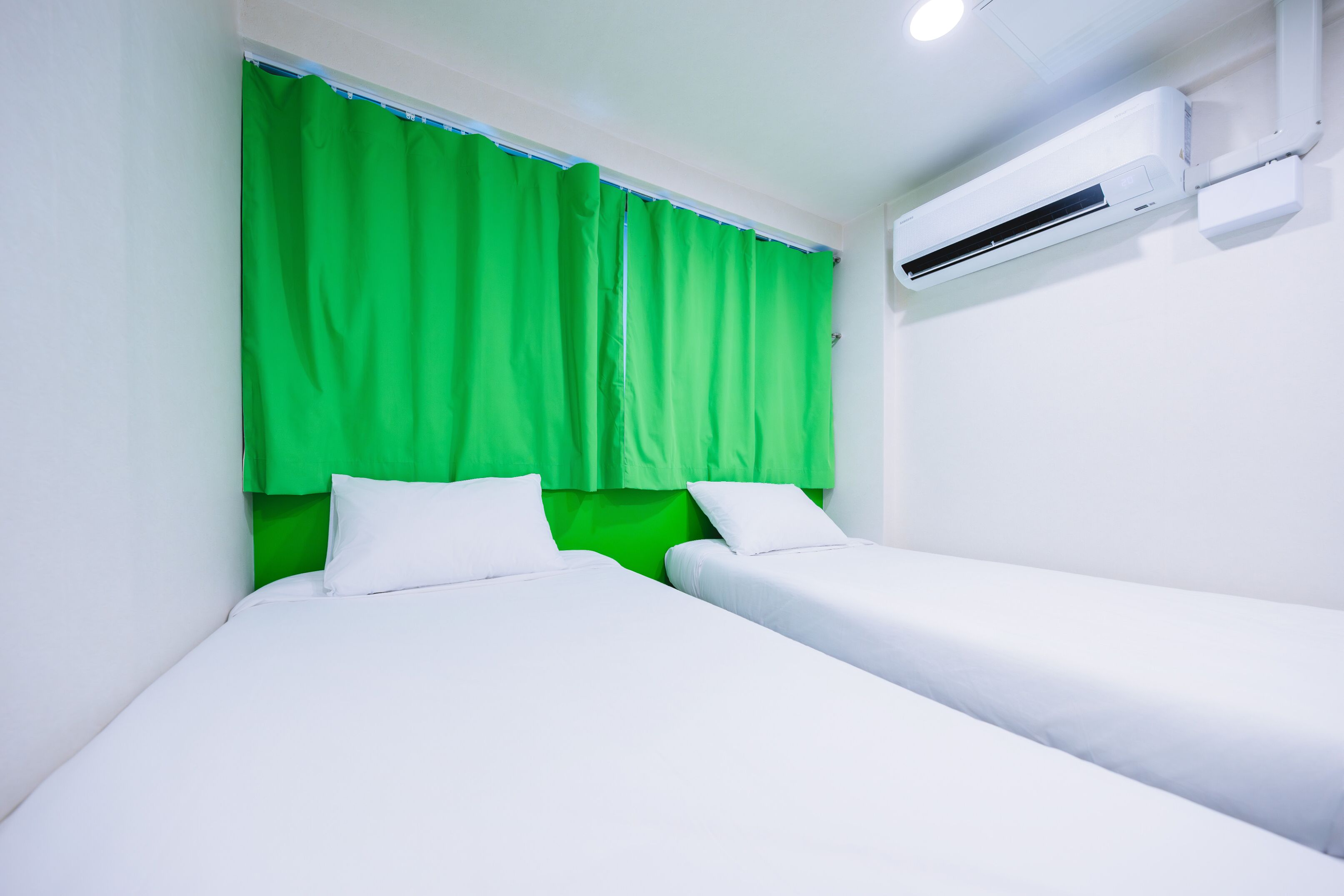 A room with two single beds, a green curtain, and an air conditioning unit on the wall.
