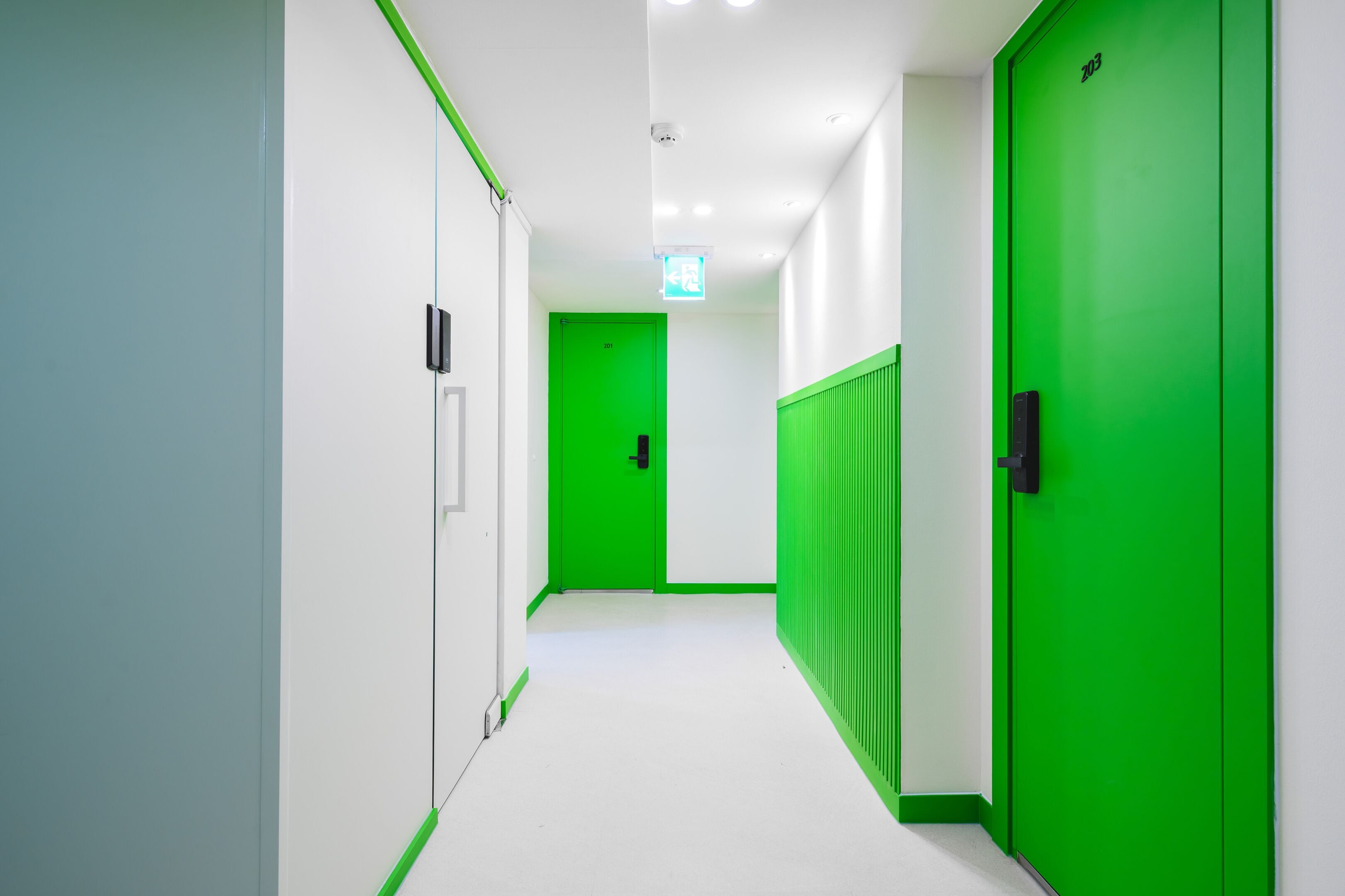 Un couloir avec des portes vertes, des murs blancs et un sol blanc.