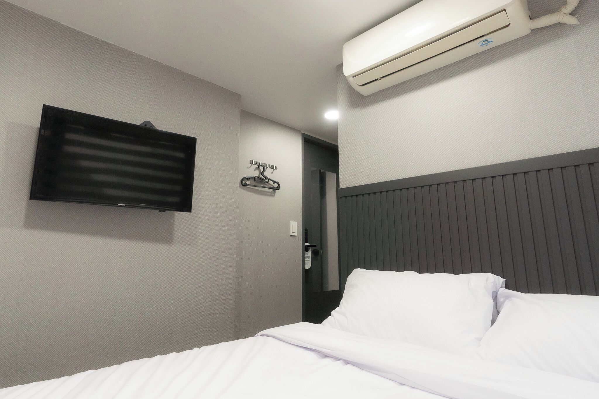 A hotel room with a bed, a mounted TV, and an air conditioning unit.