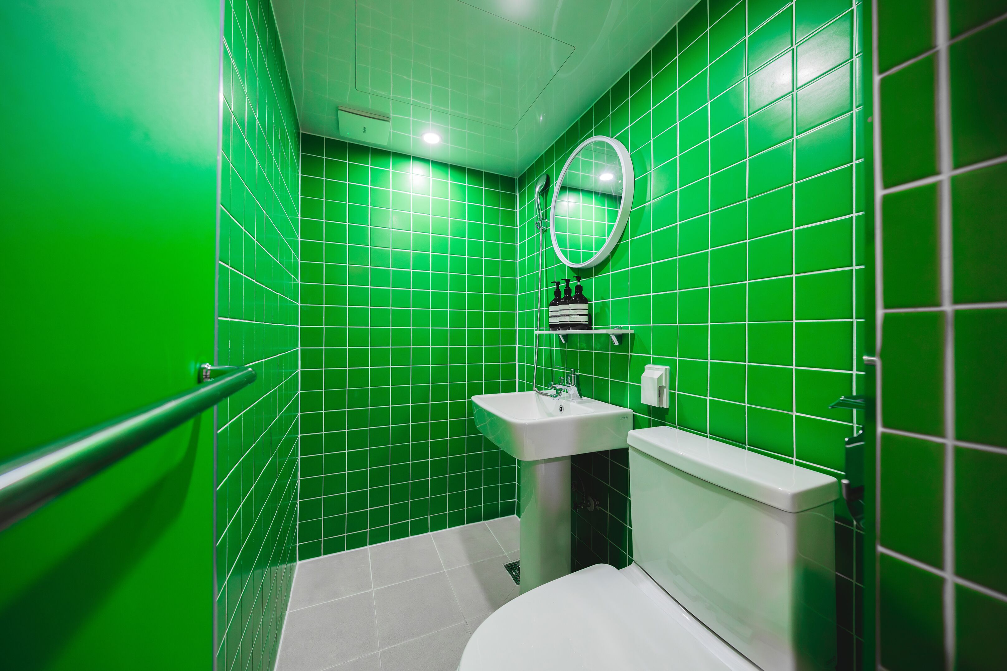 A bathroom with green tiles, a white sink, a toilet, and a mirror.