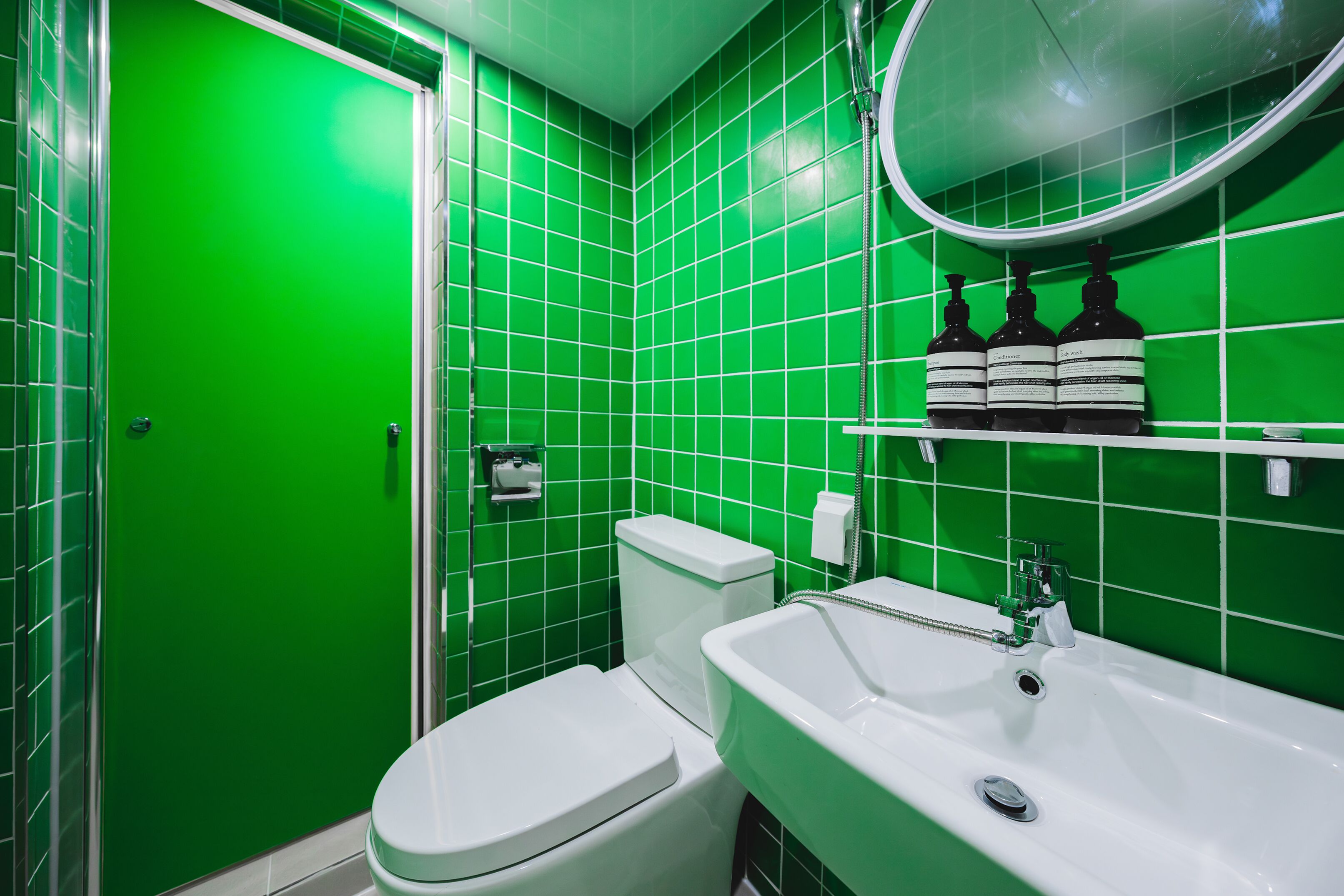 Une salle de bain avec des carreaux verts, des toilettes blanches, un lavabo blanc et un miroir au-dessus du lavabo.