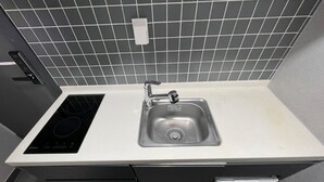 A compact kitchen with a built-in stovetop, a stainless steel sink, and a tiled backsplash. - INN THE HOUR_Myeongdong (Seoul)