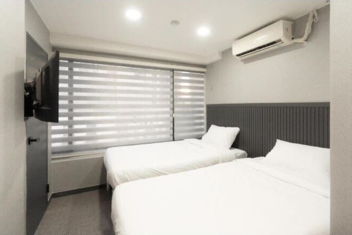 A hotel room with two beds, a TV, and an air conditioning unit.