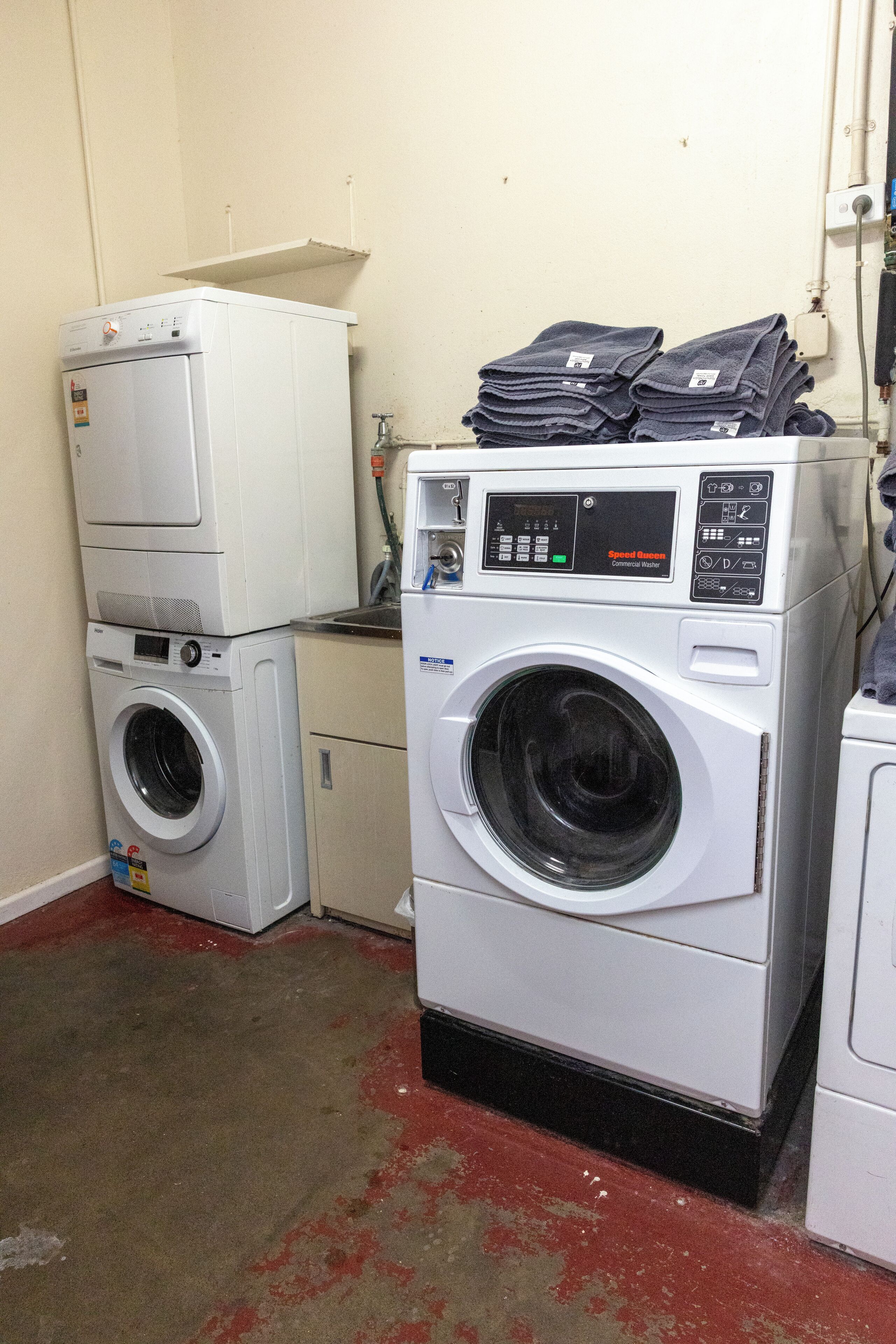 Une buanderie avec des machines à laver et des sèche-linge superposés, un sol rouge et un mur blanc.