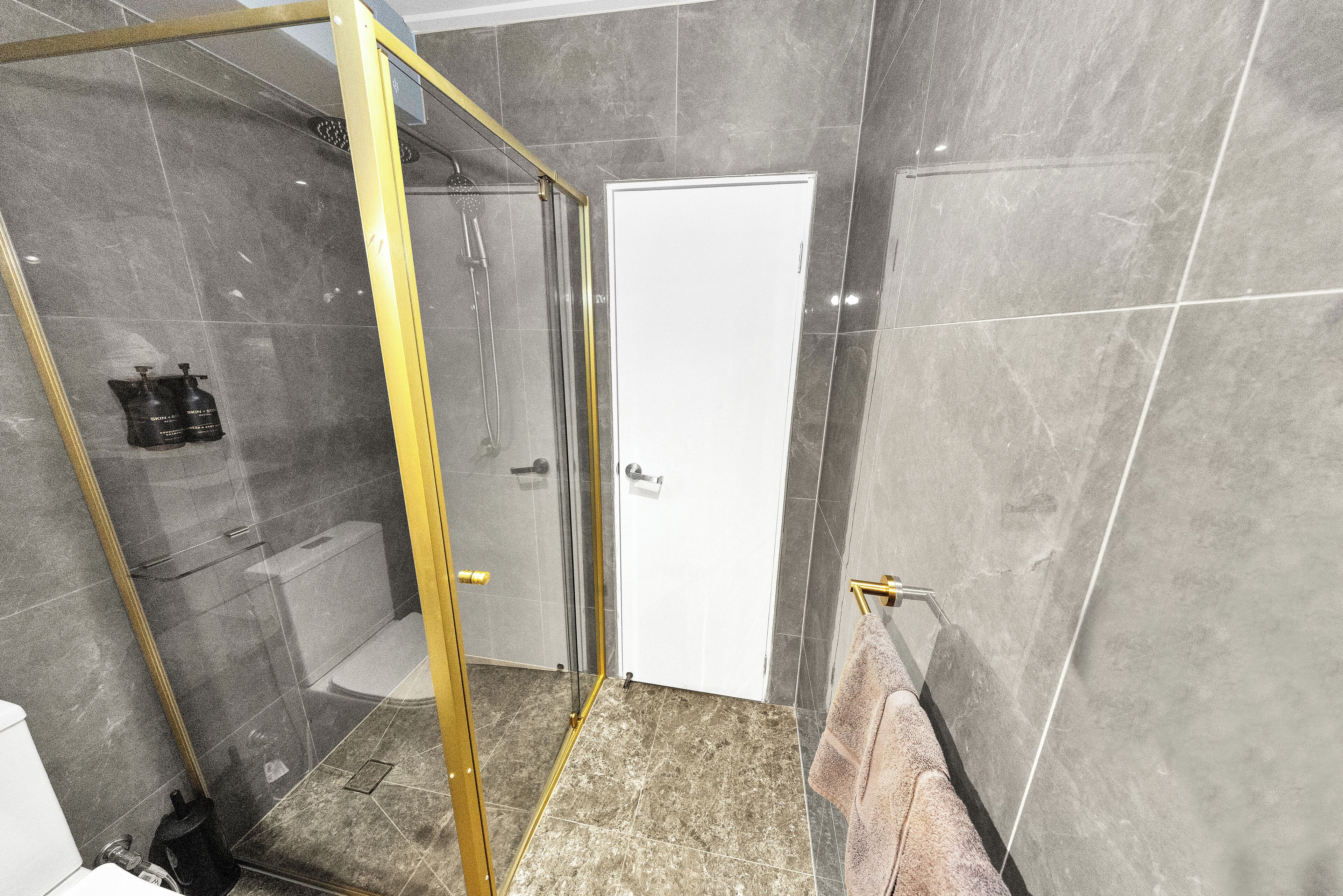 A modern bathroom with a glass-enclosed shower, a white door, and a towel rack.