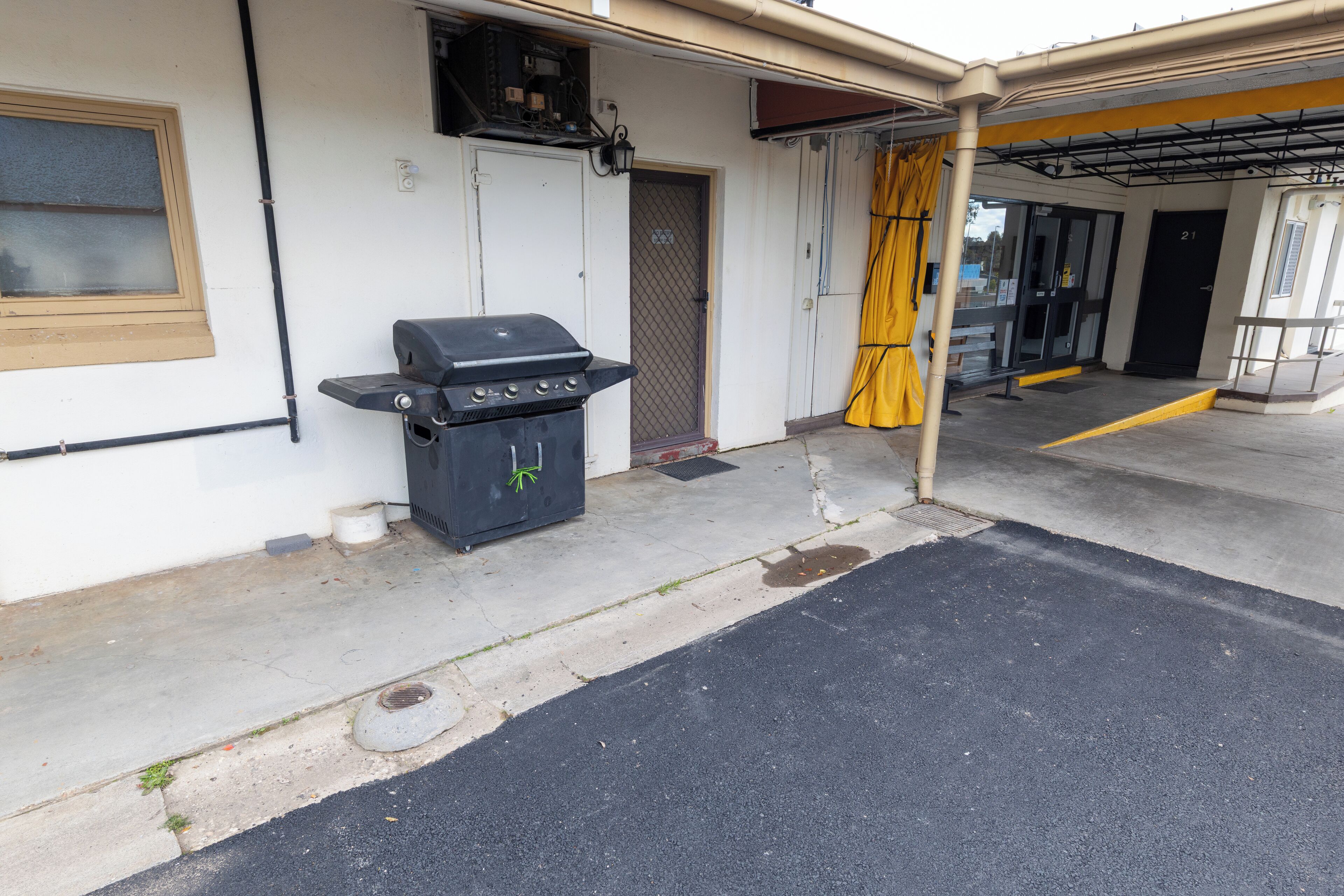 A building with a covered entrance, a grill outside, and a door marked with the number 21.