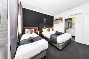 A hotel room with two beds, a dark accent wall, a framed picture, and a bathroom visible through an open door. - Golden Hills Motel  (Golden Square)