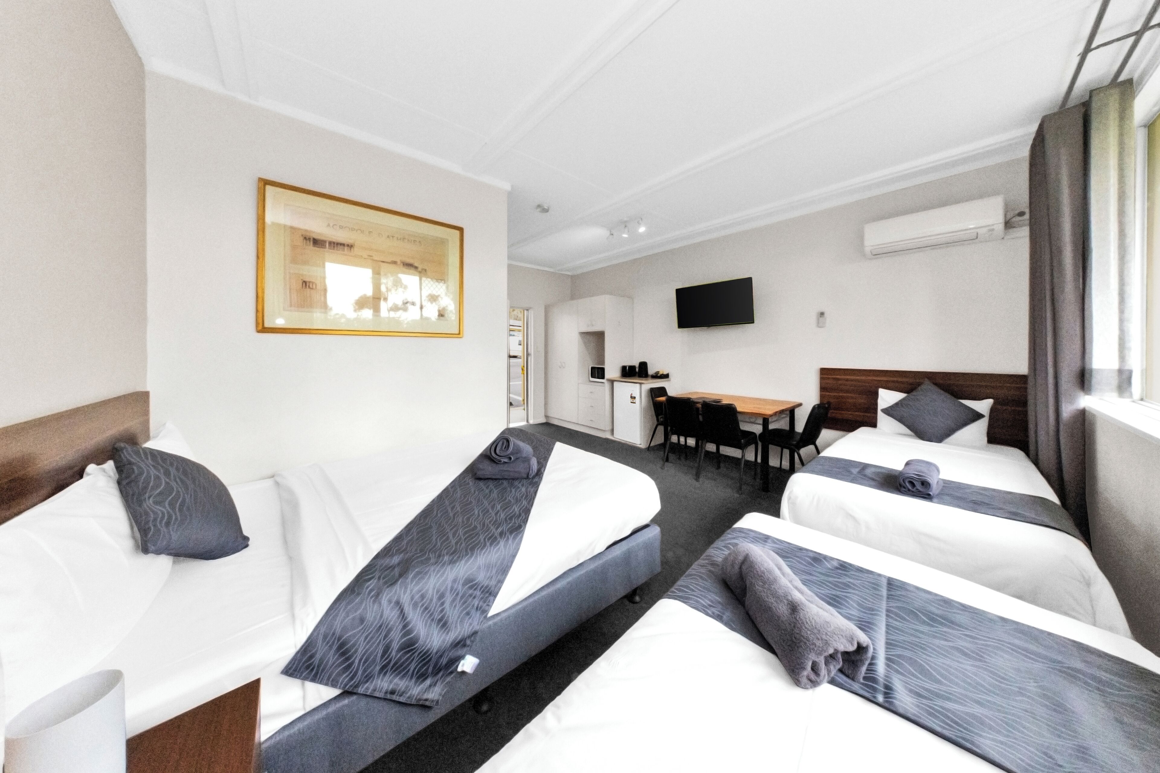 Une chambre d’hôtel avec deux lits simples, un bureau, une chaise, un téléviseur à écran plat et un appareil de climatisation.