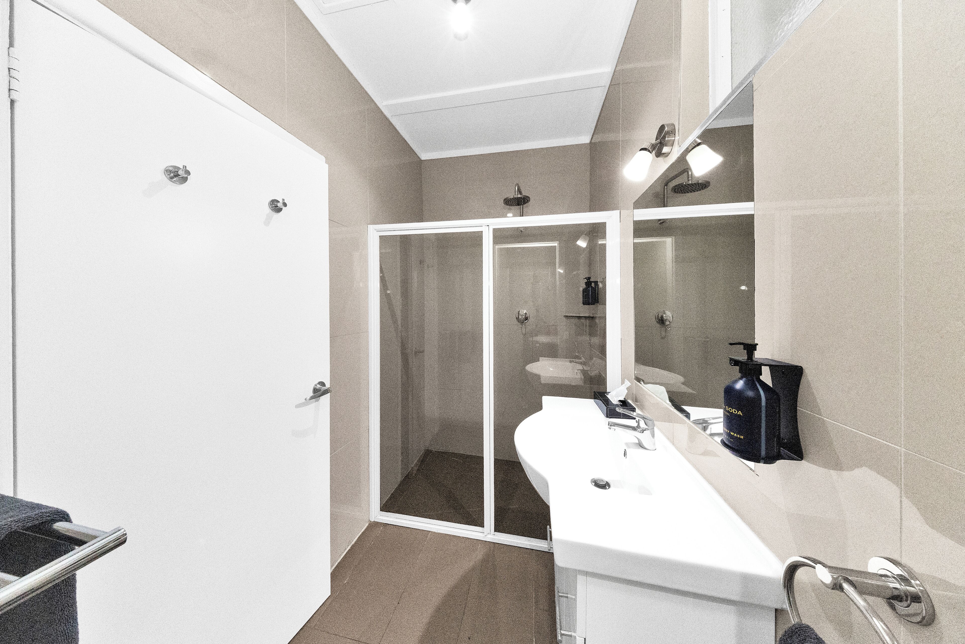 A modern bathroom with a glass-enclosed shower, a white sink, and a large mirror.