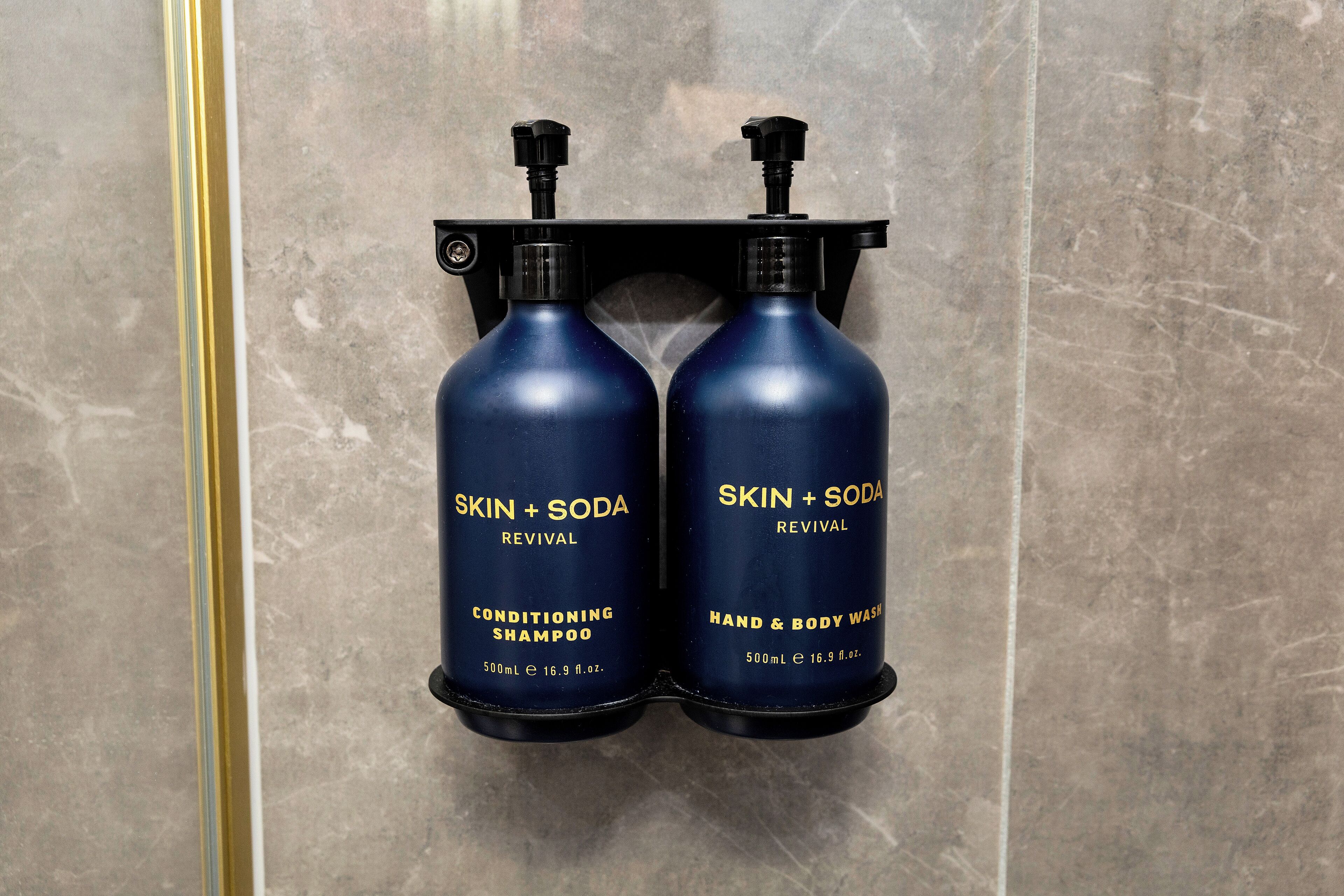 Two bottles of SKIN + SODA hand and body wash mounted on a wall.