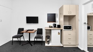 Una habitación compacta con escritorio, dos sillas, televisor, microondas y refrigerador pequeño.