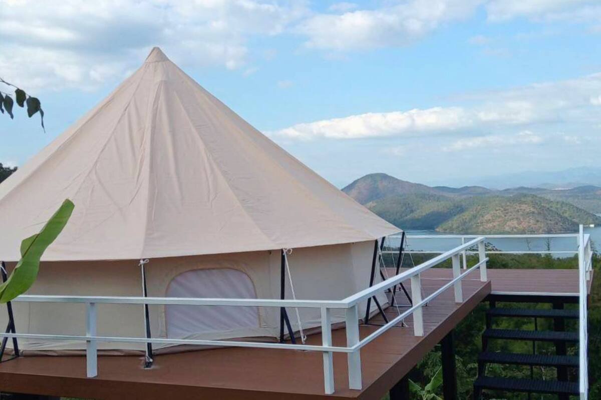 Een koepeltent met een witte reling en een houten terras, met uitzicht op een bergachtig landschap en een waterpartij.