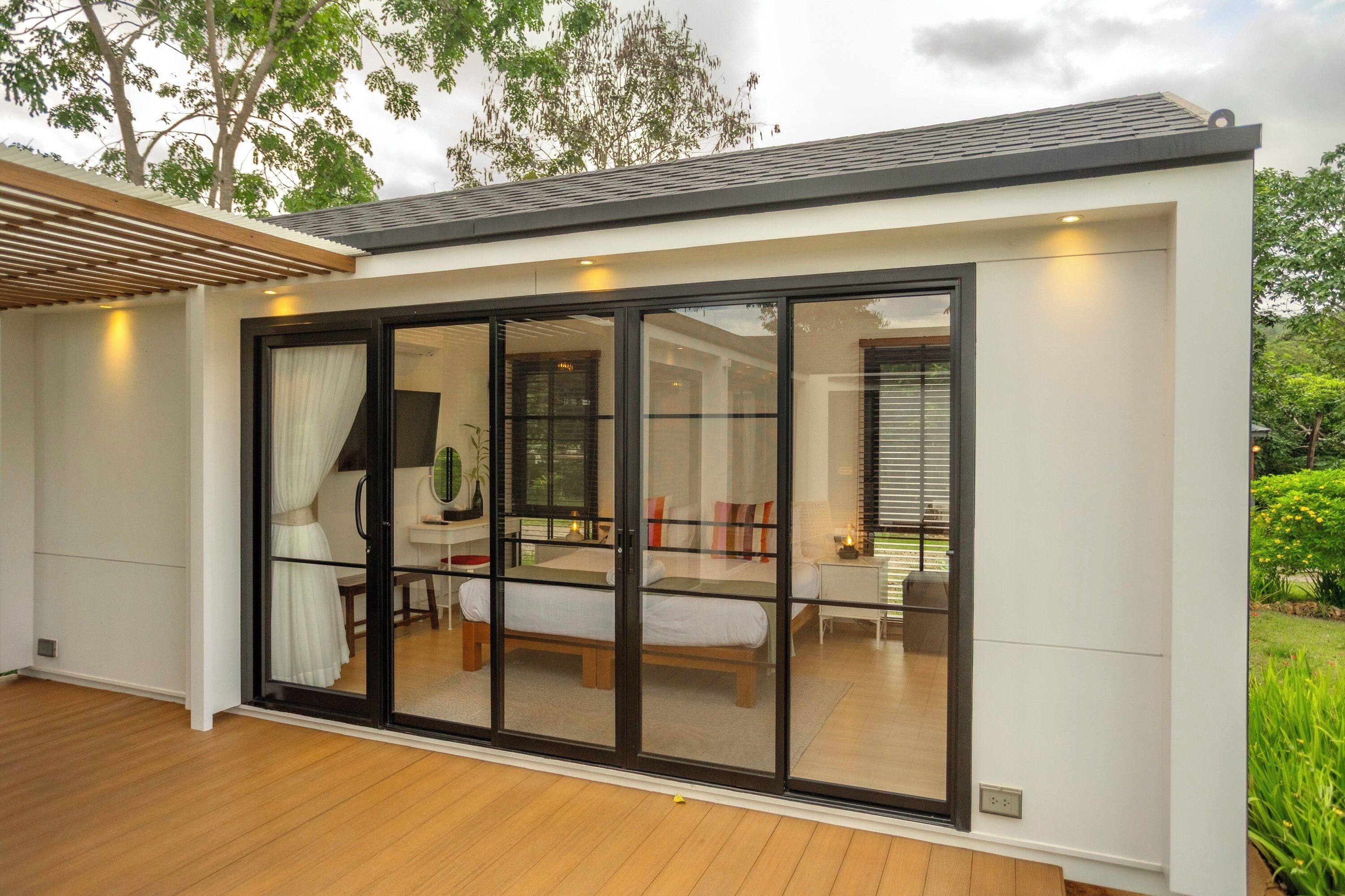 Un dormitorio moderno con un amplio ventanal corredero, una terraza de madera y vistas al jardín.