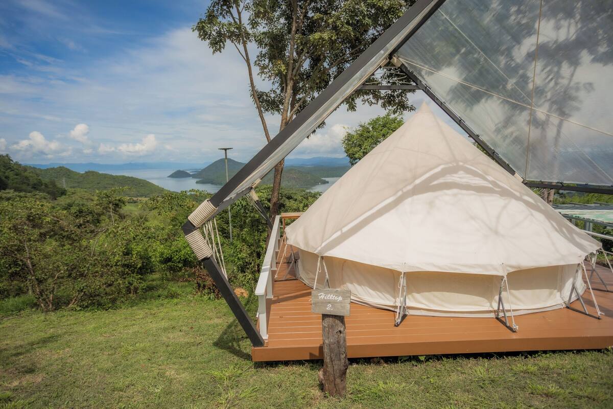 Een tent met een houten terras, omgeven door groen en een prachtig uitzicht op heuvels en water.