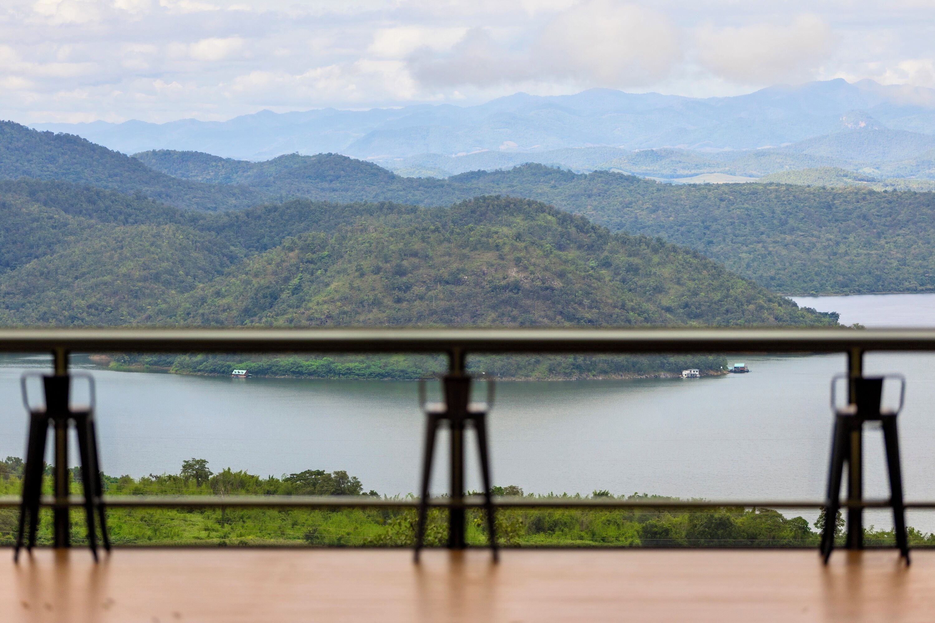 Een panoramisch uitzicht op een meer, omgeven door bergen, zichtbaar vanaf een balkon met een tafel en stoelen.