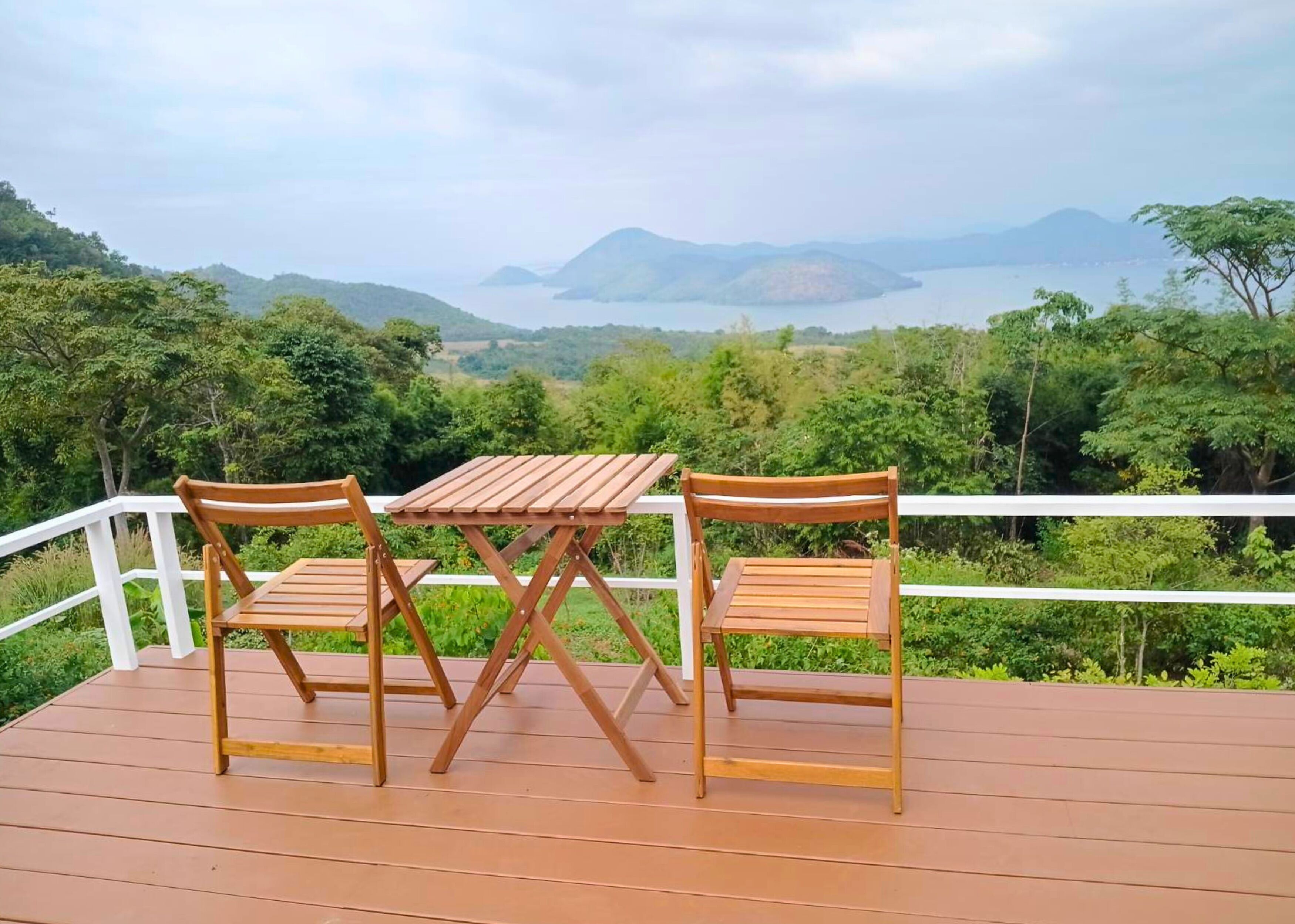 A wooden deck with a table and two chairs, overlooking a scenic landscape with hills and a body of water.