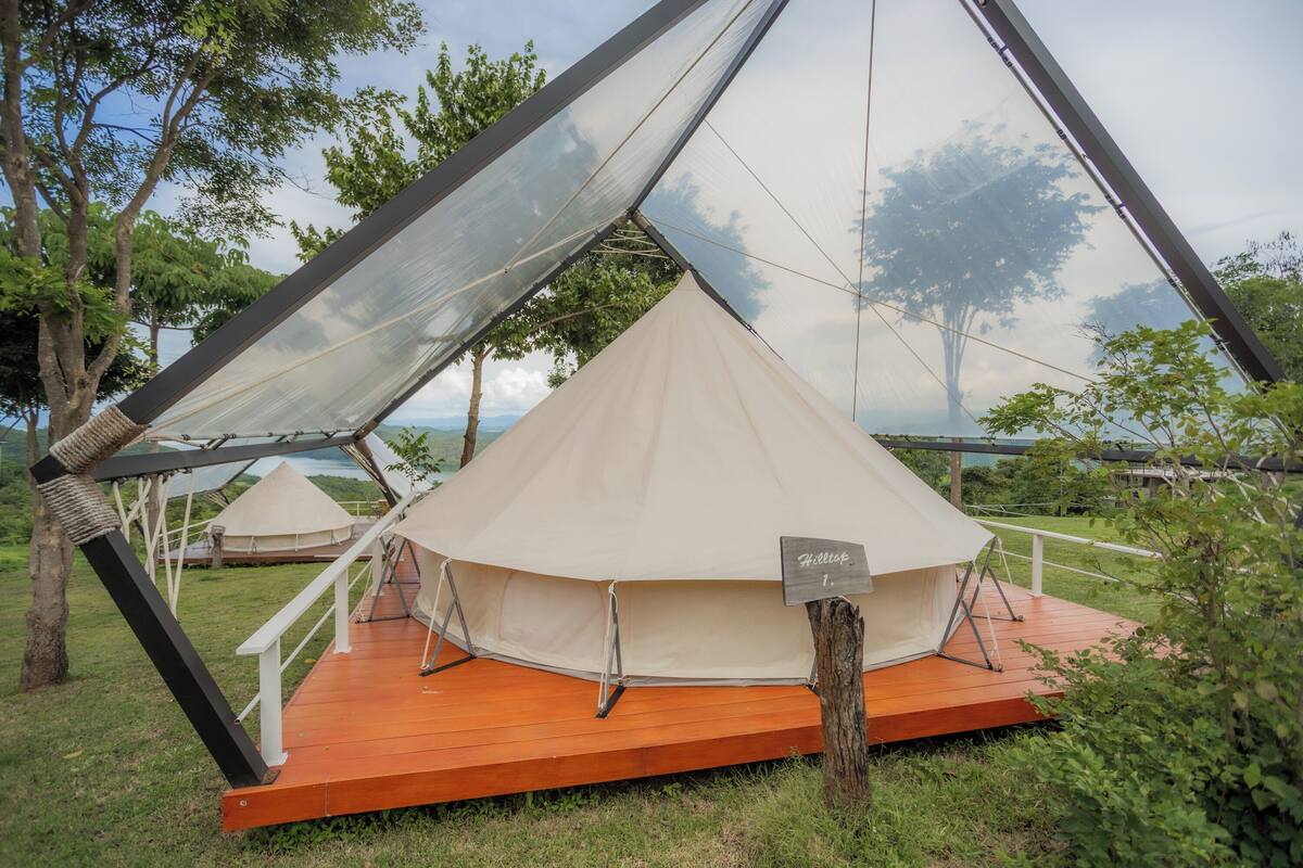 Een grote, beige tent met een houten terras en een bordje waarop staat 'Hilltop 1' accommodatie.